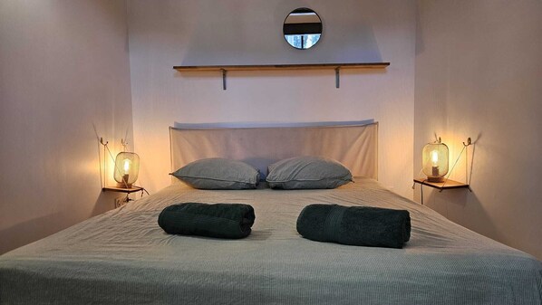 A neatly made bed with two pillows and two folded towels, flanked by two wall-mounted lamps.