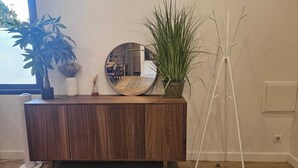 Un mueble de madera con un espejo, una planta en maceta y un pequeño jarrón con flores secas.