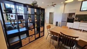 Una cocina moderna con zona de comedor, que cuenta con una estantería negra con cestas, una mesa de madera y sillas.
