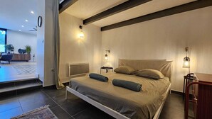 Un dormitorio moderno con cama, mesitas de noche y vistas al salón.