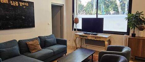 A modern living room with a large window, a black sofa, a yellow chair, and a wooden coffee table.