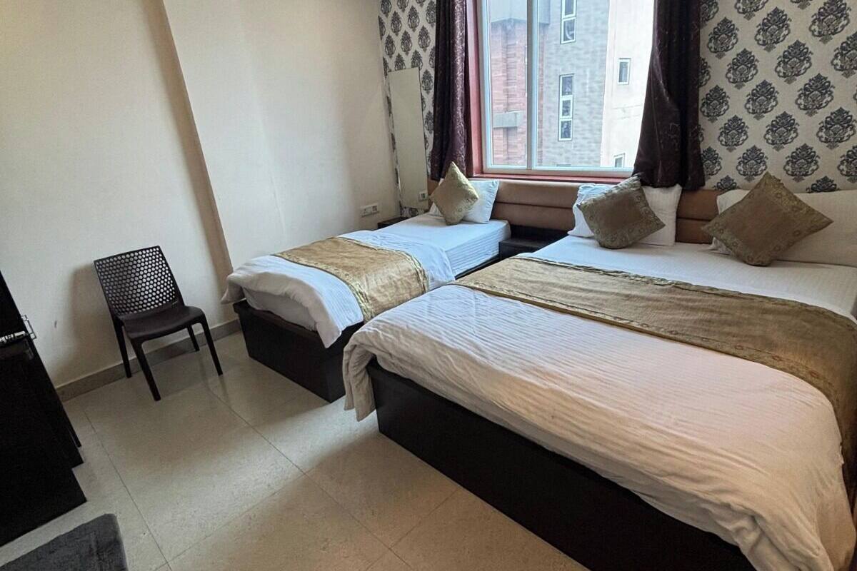 A hotel room with two beds, a ceiling fan, a window with curtains, and a view of buildings outside.
