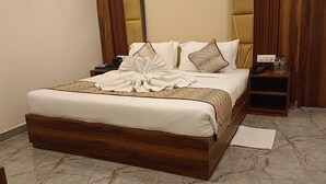 Una cama bien hecha con cabecera de madera, una mesita de noche con teléfono y lámpara, y una pequeña mesita auxiliar de madera con lámpara.