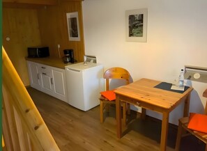 Una cocina compacta con lavadora, cafetera y una mesa con sillas.
