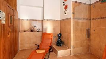 Una stanza con soffitto in legno, cabina doccia con piastrelle e una poltrona prendisole.