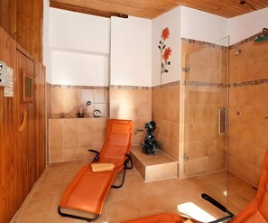 Una habitación con techo de madera, zona de ducha con azulejos y una tumbona.