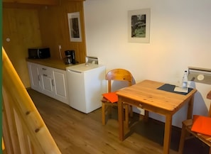 Una cocina compacta con lavadora, cafetera y una mesa con sillas.