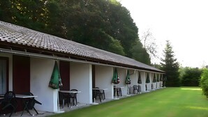 A row of outdoor tables and chairs with green umbrellas, a well-maintained lawn, and a building with a tiled roof. - Hotel Schachten – Apartment 3 mit Bergblick, Frühstück inklusive & Shuttleservice (Lindberg)