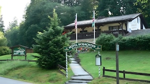 A hotel entrance with a sign reading 'HOTEL SCHACHTEN,' a pathway leading to the building, and a wooden fence. - Hotel Schachten – Apartment 3 mit Bergblick, Frühstück inklusive & Shuttleservice (Lindberg)