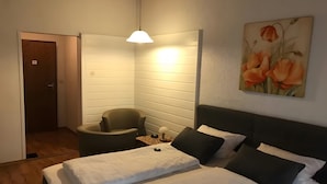 Ett sovrum med en säng, en stol, ett skrivbord och en tavla på väggen.