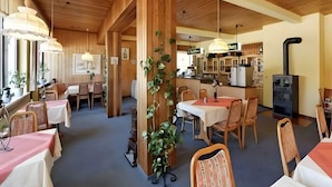 En restaurang med träinredning, bord med vita och röda dukar och ett kök synligt i bakgrunden.