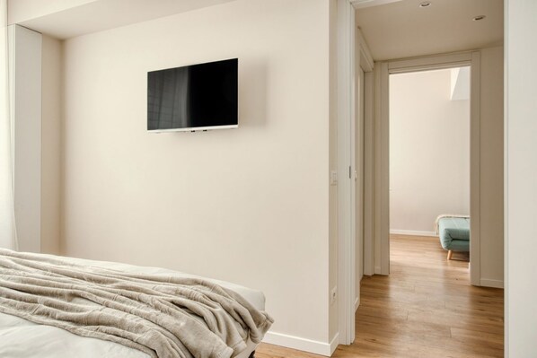 A bedroom with a bed, a TV mounted on the wall, and a door leading to another room.