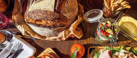 A wooden table with a variety of food items including bread, cheese, tomatoes, and cured meats.