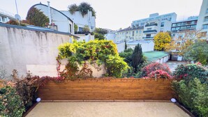 Une terrasse sur le toit, avec un banc et des chaises en bois, entourée d’une végétation luxuriante et offrant une vue sur les bâtiments de la ville.