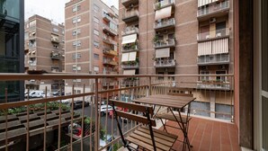 A balcony with a table and chairs, overlooking a street with cars and buildings. - GuestHost - Trastevere Apartment Roma Portuense (Rome)