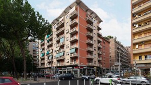 A multi-story building with balconies, a ground-floor shop, and parked cars. - GuestHost - Trastevere Apartment Roma Portuense (Rome)