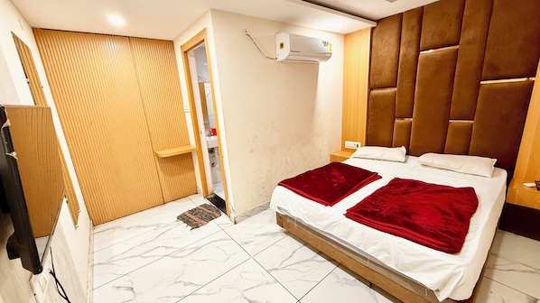 Un dormitorio con cama, armario de madera, unidad de aire acondicionado y puerta de baño.