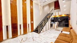 Un moderno vestíbulo de hotel con piso de mármol, una escalera, una recepción y un área de descanso.