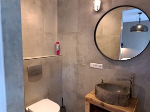 Et badeværelse med en sten-vask, et rundt spejl, et toilet og en bruseplads.