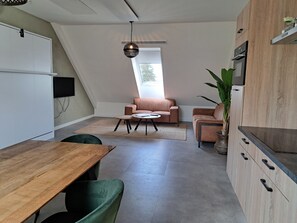 Et moderne loftrum med spiseplads, siddeområde, køkken og et stort vindue.
