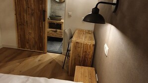A bedroom with a bed, a wooden desk, a wall-mounted lamp, and a sliding door.