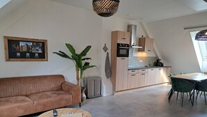 A modern living room with a sofa, two round tables, a potted plant, and a kitchen in the background.