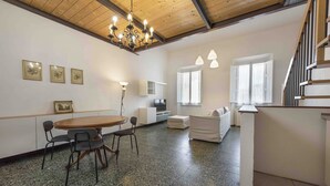 Amplia sala de estar con techo de madera, una mesa de comedor con sillas, un sofá y una escalera.