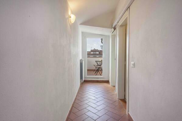 A narrow hallway with a tiled floor leading to a door with a view of a balcony. - San Zanobi panoramic terrace by MMega (Florence)