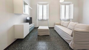 Una sala de estar moderna y minimalista con sofá, reposapiés, televisor y armario empotrado.
