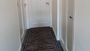 Un couloir dont le sol est recouvert de carreaux imitant des briques, avec des murs blancs et une porte fermée au bout.