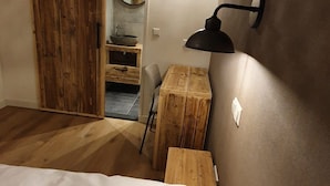 Une chambre à coucher avec un lit, un bureau en bois, une lampe fixée au mur et une porte coulissante.
