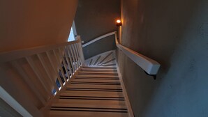 Un escalier en bois avec une rampe, un luminaire fixé au mur et une vue sur l’étage inférieur.