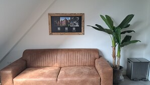 Un canapé marron, un tableau encadré, une grande plante verte et un petit appareil électroménager.