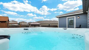 Een achtertuin met een jacuzzi, een houten terras en een huis op de achtergrond.