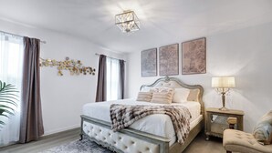 Een slaapkamer met een groot bed, een nachtkastje, een stoel en wanddecoratie.
