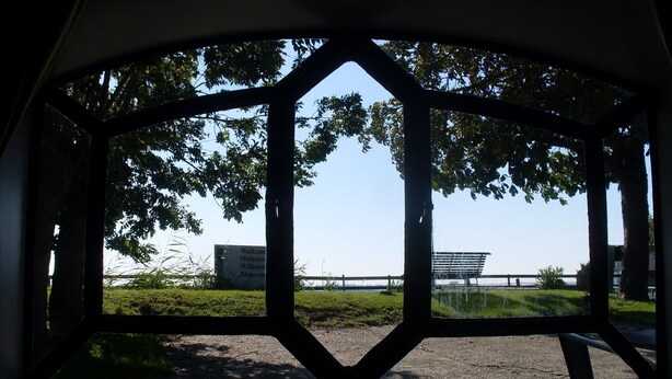 A view through a window with a geometric frame, a grassy area, a bench, and a building in the distance.