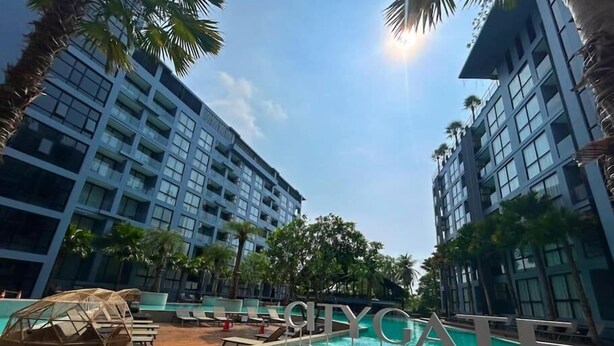 A pool area with lounge chairs and a wooden deck, surrounded by tall buildings and palm trees. - Steps to Kamala Beach Rooftop Pool  C138 (Kamala)