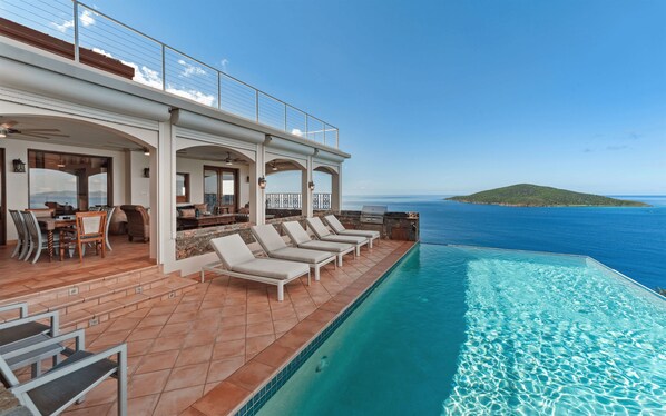 Un espace aménagé au bord de la piscine, avec des chaises longues, une table à manger et une vue sur la mer.