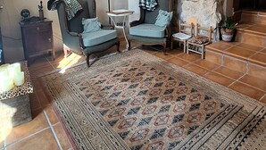 Una habitación rústica con paredes de piedra, una alfombra estampada, dos sillones, una mesita y una lámpara.