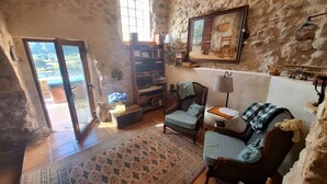 Una sala de estar acogedora con una pared de piedra, una estantería, un tablero de ajedrez y vistas a través de un ventanal.