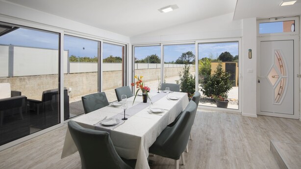 A dining area with a long table set for four, large windows, and a view of the outside. - Holiday Estate Stancija Matošić in Medulin (Medulin)