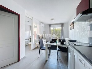 Kompakti keittiö, jossa on ruokailutila, suuri ikkuna ja ovi, joka johtaa toiseen huoneeseen.
