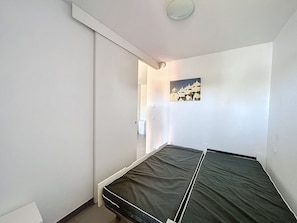 A small, single-bed room with a sliding door, a ceiling light, and a wall-mounted picture.