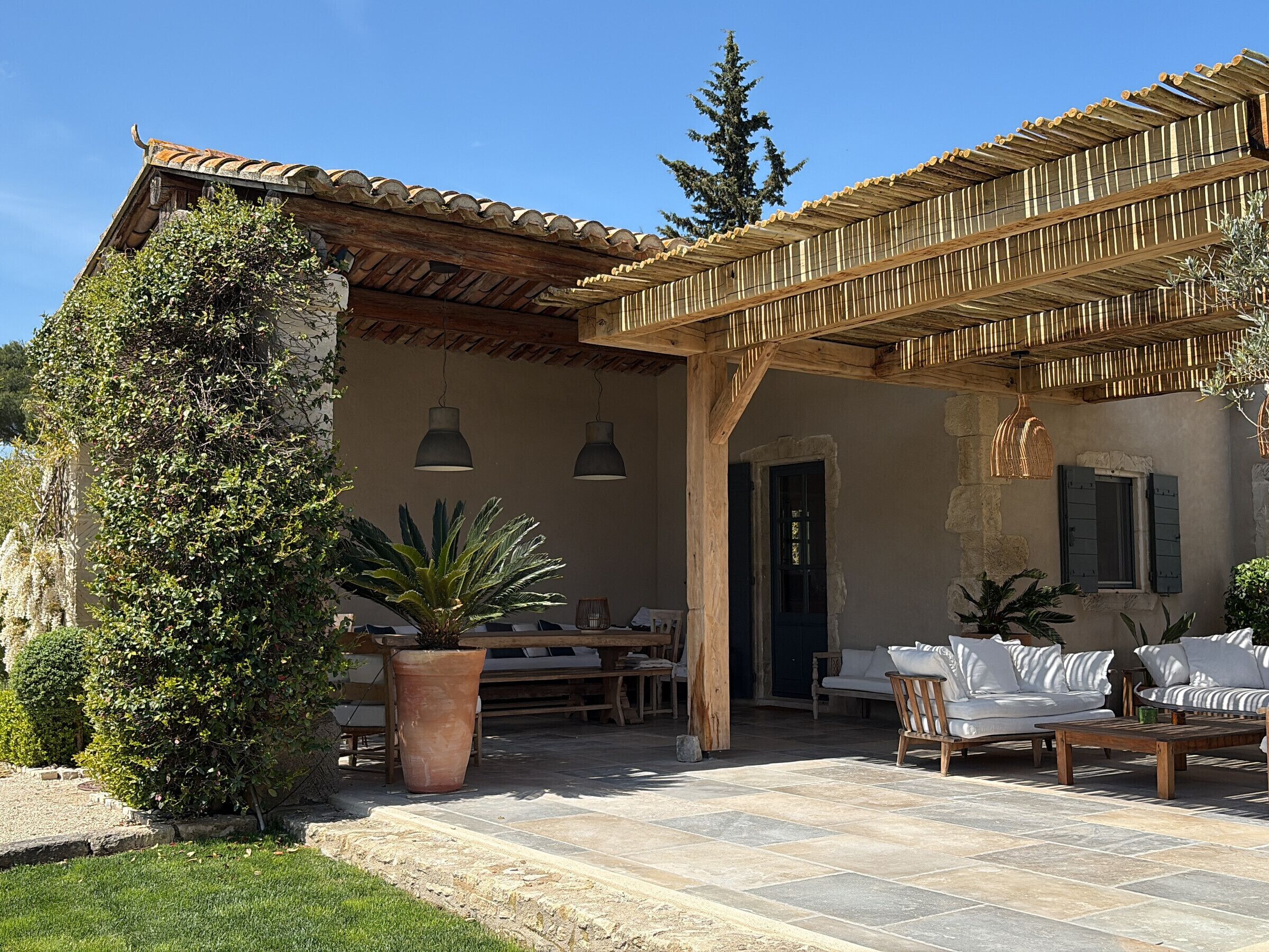 Une terrasse extérieure dotée d’une pergola en bois, d’un sol en pierre et d’un espace salon avec des canapés blancs et une table.