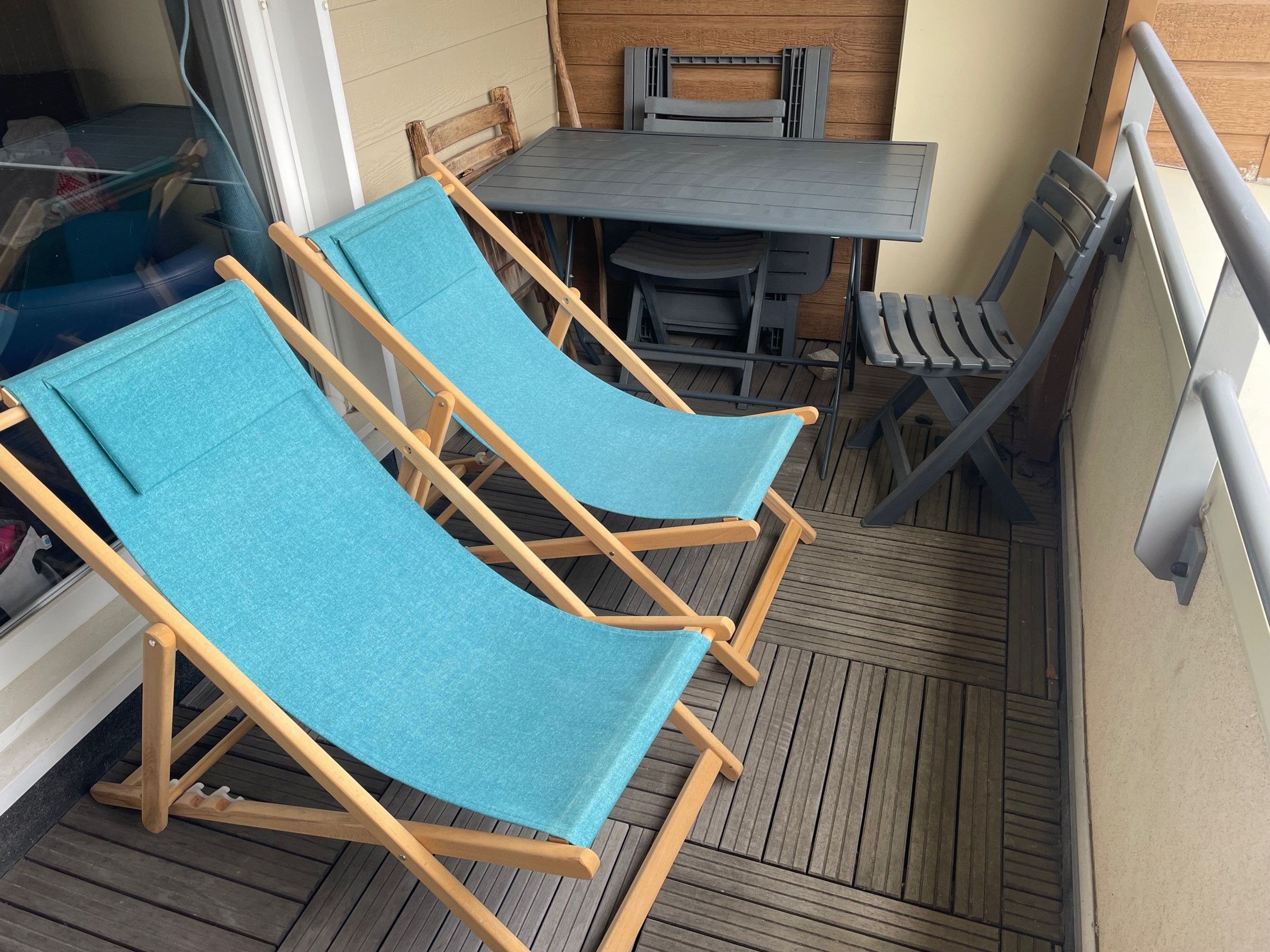 A wooden deck with two blue lounge chairs, a table, and chairs.
