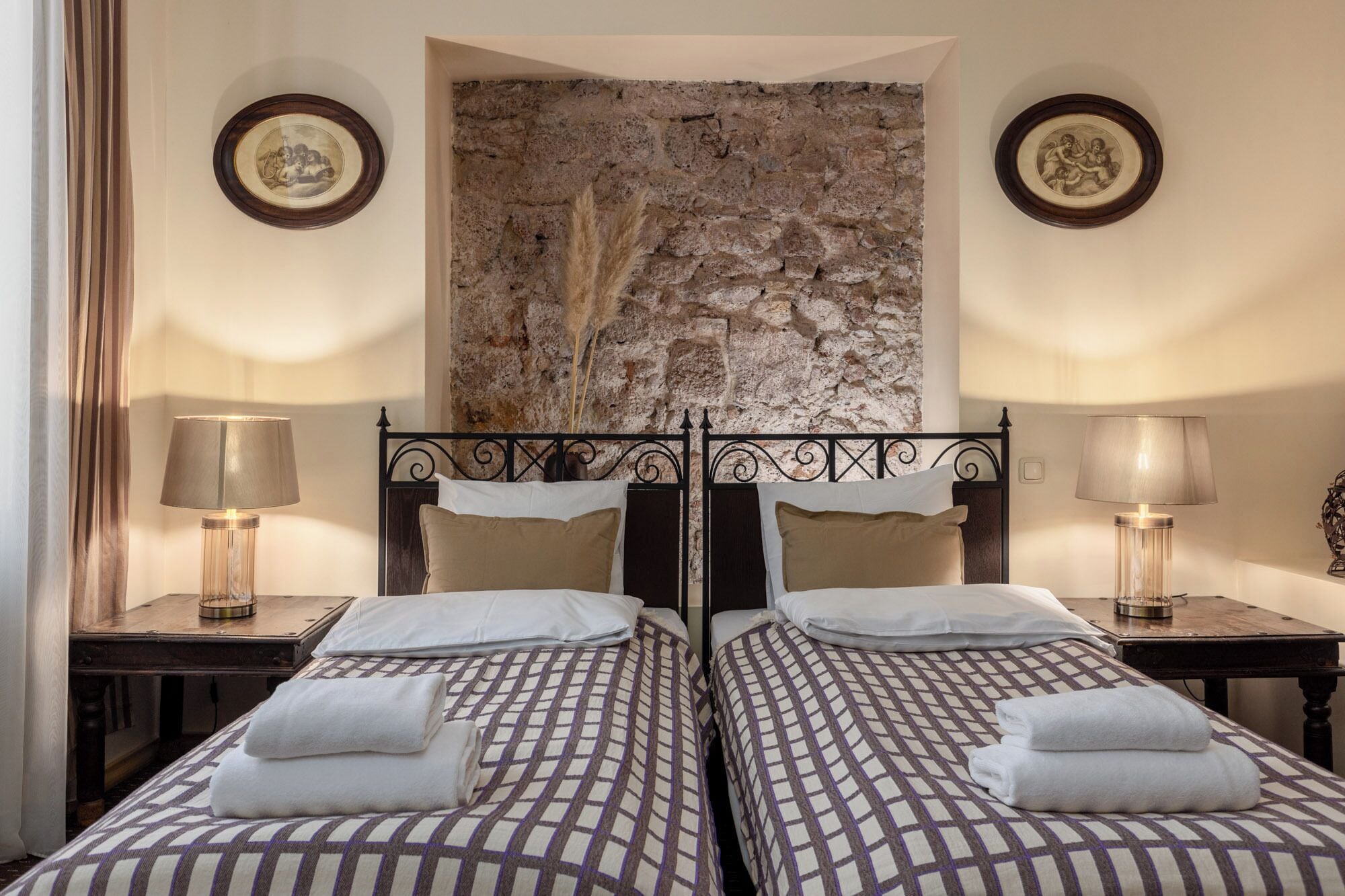 Una cama doble con una colcha estampada, dos mesitas de noche con lámparas, una pared de piedra y cuadros enmarcados en las paredes.