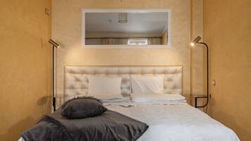 A bedroom with a tufted headboard, a bed with white bedding, a dark throw pillow, and two floor lamps.