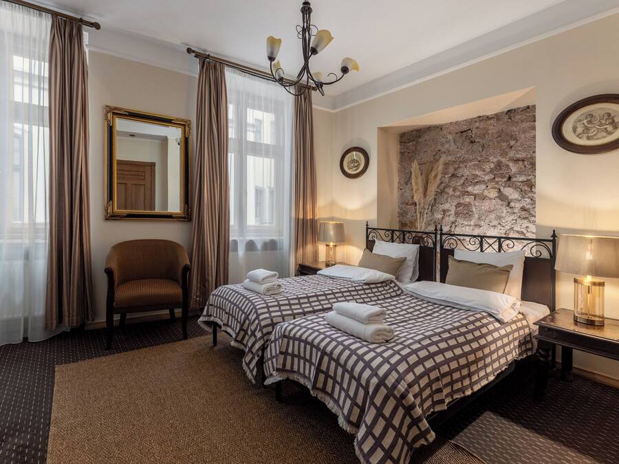 Habitación de hotel con dos camas, una silla, un candelabro y una pared de piedra.