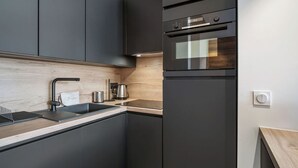 A modern kitchen with dark cabinetry, a stainless steel sink, and a built-in oven. - Family duplex near Courchevel slopes with wifi and parking (Courchevel 1650)