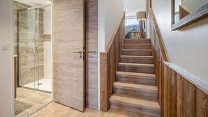 A modern interior with a wooden staircase, a glass shower enclosure, and a view of the outdoors. - Family duplex near Courchevel slopes with wifi and parking (Courchevel 1650)